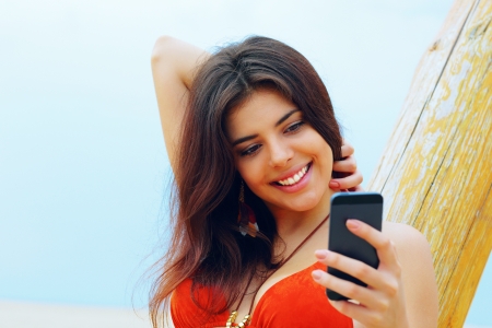 Happy young woman using her smartphone on the beachの写真素材