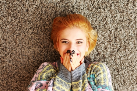 Laughing young woman lying on the carpet at homeの写真素材