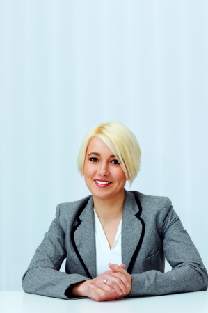Young cheerful businesswoman in casual cloth sitting at the table in officeの写真素材