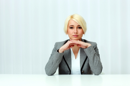 Young beautiful pensive businesswoman sitting at the table in officeの写真素材