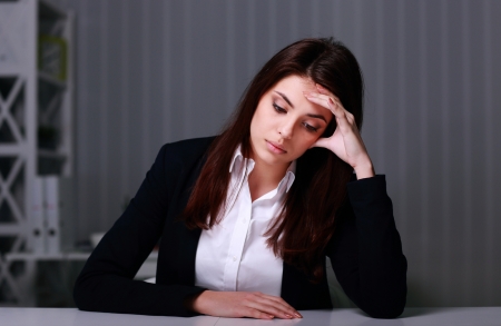 Young sad businesswoman sitting at the table on her workplace in officeの写真素材