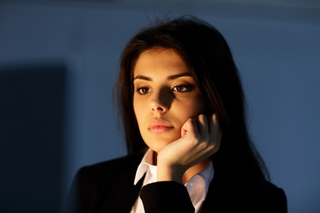 Closeup portrait of a young tired businesswoman working at night. Looking at laptop.の写真素材