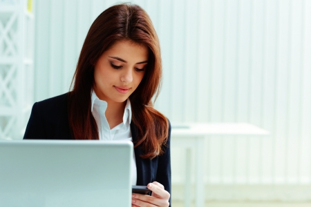 Young businesswoman looking at smartphone on her workplace in officeの写真素材