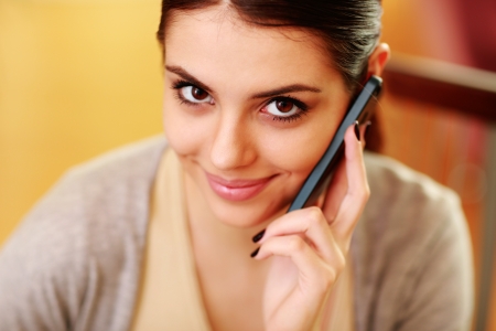 Closeup portrait of a young happy woman talking on a phone at homeの写真素材