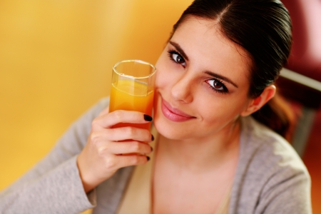Young beautiful happy woman holding glass of orange juice at homeの写真素材