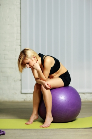 Young pensive fit woman sitting on the fitballの写真素材