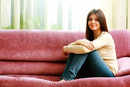 Young happy smiling woman sitting on the sofa at homeの写真素材