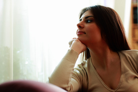 Young beautiful woman looking on a window at homeの写真素材