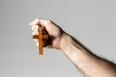 Male hand holding wooden cross on gray backgroundの写真素材