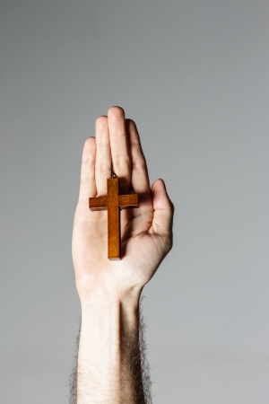 Male hand holding wooden cross on gray backgroundの写真素材