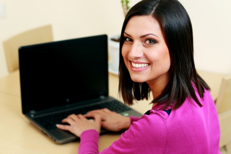 Young happy woman typing on the laptop and looking at cameraの写真素材