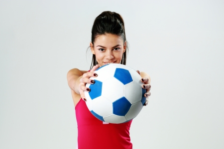 Young happy sport woman giving you a soccer ball on gray backgroundの写真素材