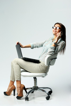 Young happy businesswoman using laptop and phone on gray backgroundの写真素材