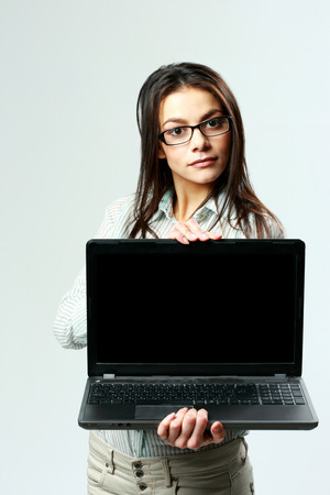 Young beautiful businesswoman showing laptop on gray の写真素材