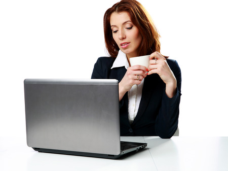 Pensive businesswoman sitting on the table with laptop and drinking coffee isolated on a white backgroundの写真素材