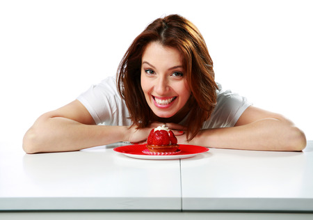 Happy woman sitting on the table with fresh strawberry cake isolated on a white backgroundの写真素材