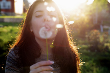Beautiful woman blowing on dandelion in the gardenの写真素材