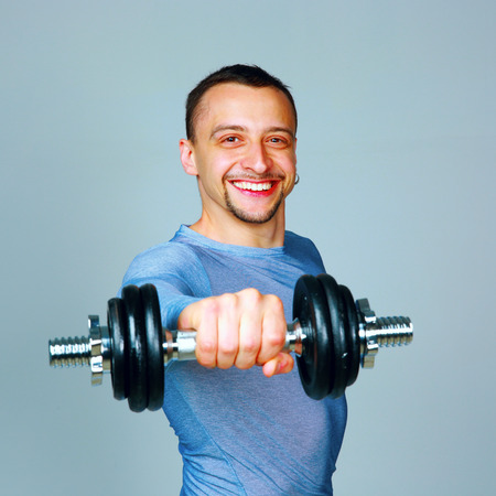 Happy man working out with dumbbells over grayの写真素材