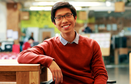 Young cheerful asian student sitting at the tableの写真素材