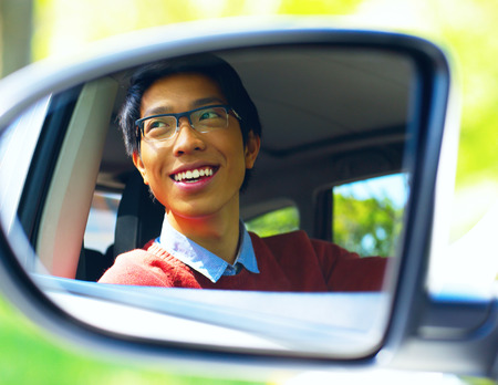 Smiling asian driver is reflected in mirror of carの写真素材