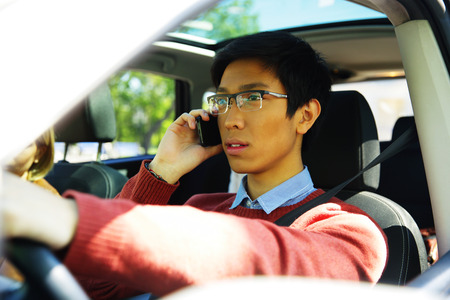 Young asian man driving car and talking on mobile phoneの写真素材
