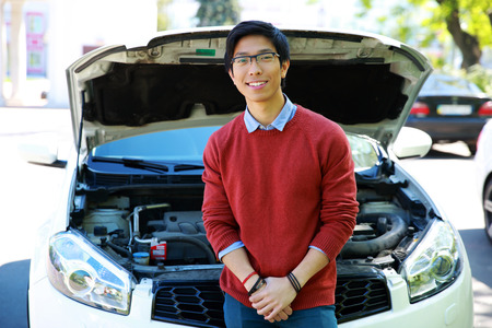 Young asian man standing near car with bonnet openの写真素材