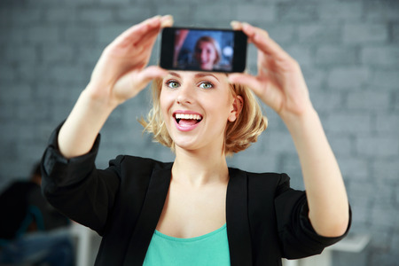 Young laughing woman making a self photo by her smartphone in office