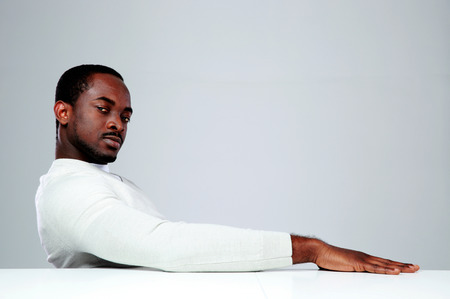 Thoughtful african man sitting at the table on gray backgroundの写真素材