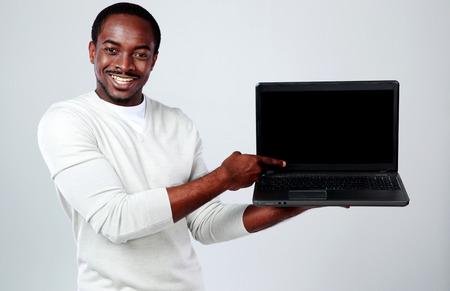 Portrait of african man showing blank laptop screen on gray backgroundの写真素材