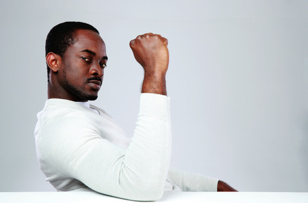 Serious african man sitting at the table on gray backgroundの写真素材