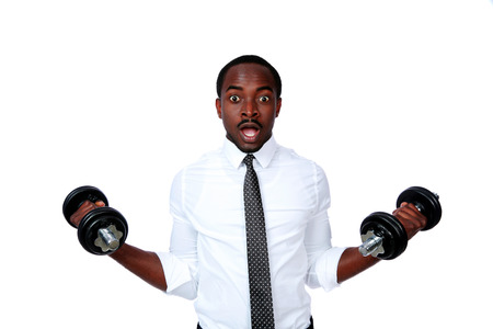 Portrait of a surprised african businessman lifting dumbbells on white backgroundの写真素材