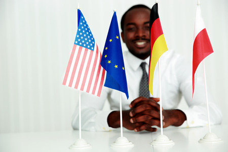 Happy businessman sitting at the table at his workplace. Focus on flagsの写真素材