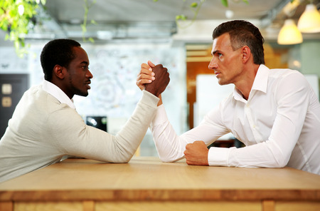 Portrait of two businessmen sitting opposite each other elbowing on the table with their arms...
