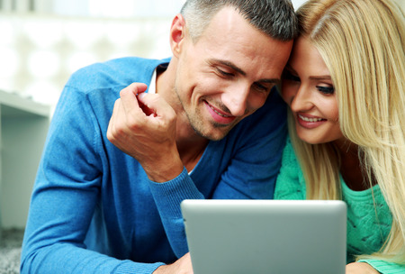 Young couple lying on the carpet and using tablet computer togetherの写真素材