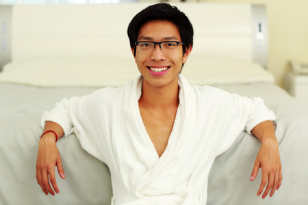 Happy man in bathrobe leaning on the bed in bedroomの写真素材