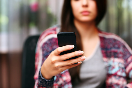 Serious beautiful woman using smartphone at home. Focus on smartphoneの写真素材