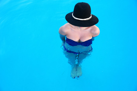 Full length portrait of a woman with hat standing in swimming poolの写真素材