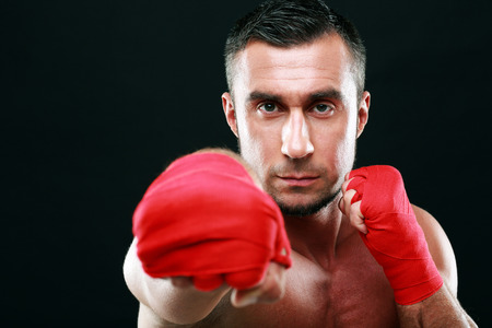 Portrait of a muscular man punching camera on black background