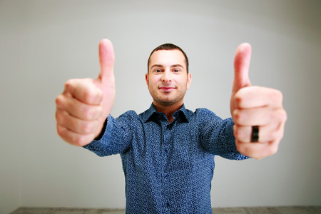Portrait of a happy man with thumbs up over gray backgroundの写真素材