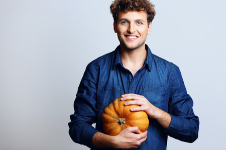 Portrait of a smiling man holding pumpkin over blue backgroundの写真素材