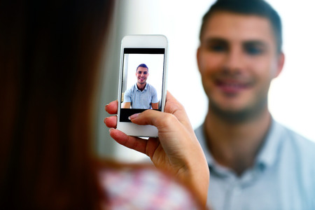 Woman making photo of a man on smartphone. Focus on smartphoneの写真素材