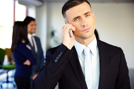 Confident businessman talking on the phone in officeの写真素材