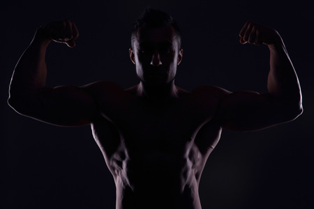 Silhouetted muscular man showing his bicepsの写真素材