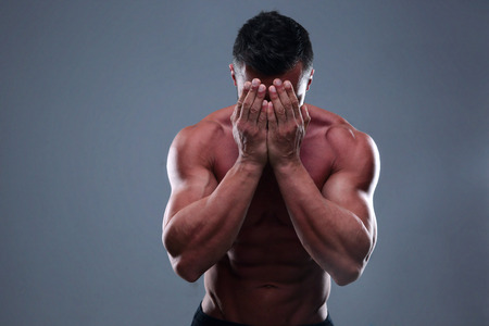 Muscular man covering his face with the hands