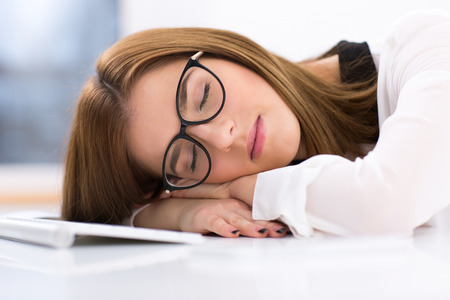 Tired businesswoman in glasses sleeping on the table at her workplaceの写真素材