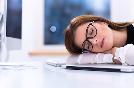 Young businesswoman in glasses sleeping at her workplaceの写真素材