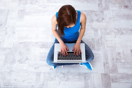 Top view portrait of a young woman sitting on the floor and typing on laptopの写真素材