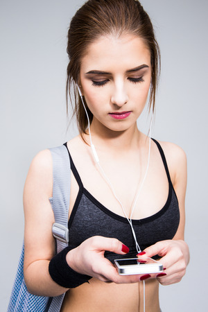 Sports woman using smartphone with headphones over gray backgroundの写真素材