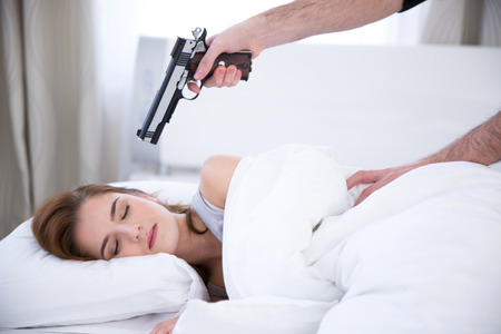 Young woman sleeping while the gun aimed at herの写真素材