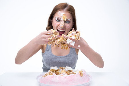 Angry young woman sitting at the table with cake at her faceの写真素材